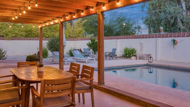An outdoor patio with a wooden table and chairs, a pool, and lounge chairs. - Mid-Century Oasis w/ heated Pool (Tucson)