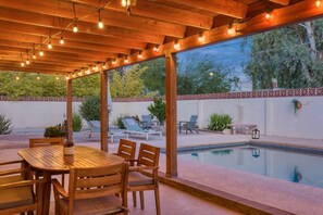 An outdoor patio with a wooden table and chairs, a pool, and lounge chairs. - Mid-Century Oasis w/ heated Pool (Tucson)