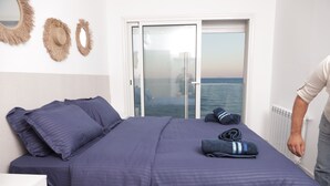 Un dormitorio con cama, cómoda y vista al mar a través de una puerta corrediza, con una persona de pie cerca de la puerta.