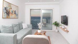Una sala moderna con un sofá gris, una mesa de centro de madera y vista al mar a través de una puerta de cristal.