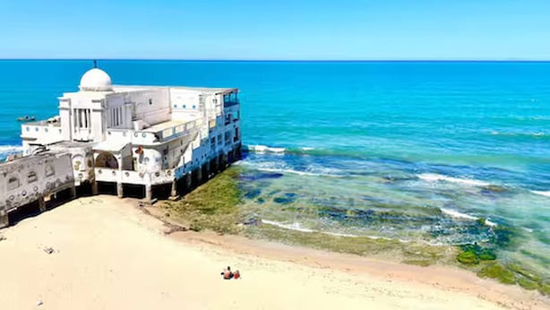 Un edificio blanco con una cúpula, ubicado en una playa con aguas azules cristalinas.