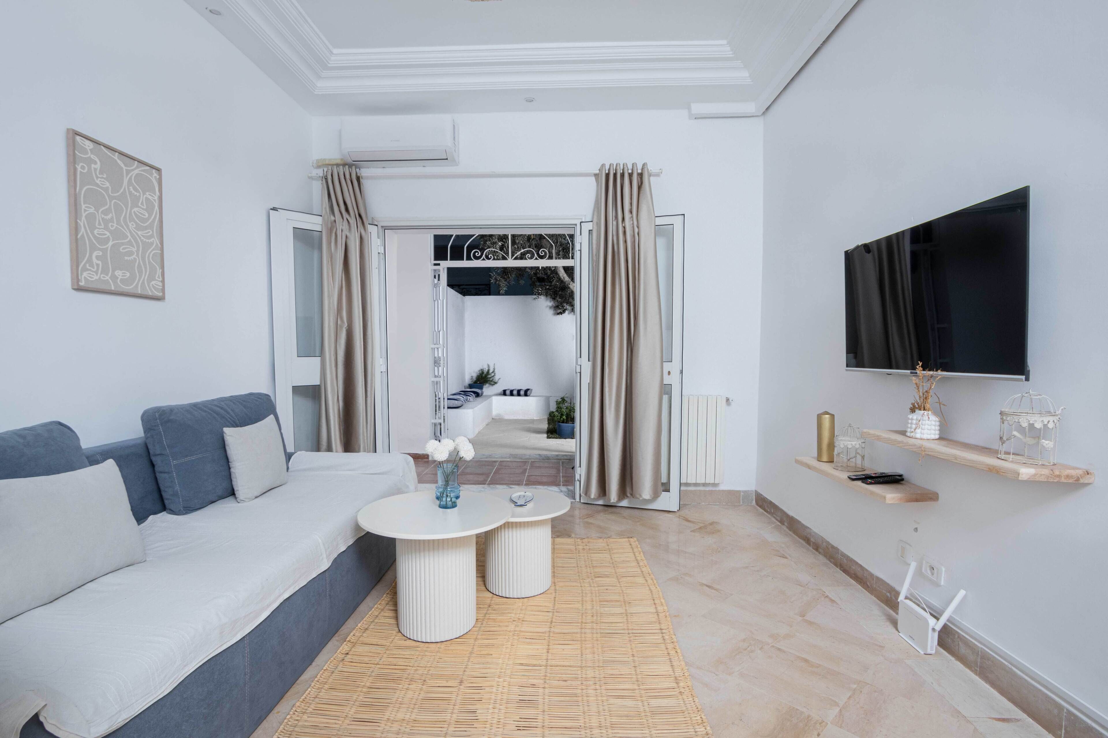 Una sala de estar moderna con un sofá, dos mesitas auxiliares, un televisor y vistas a otra habitación.
