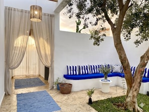Una zona relax esterna moderna con un muro bianco, cuscini a righe blu e un albero.