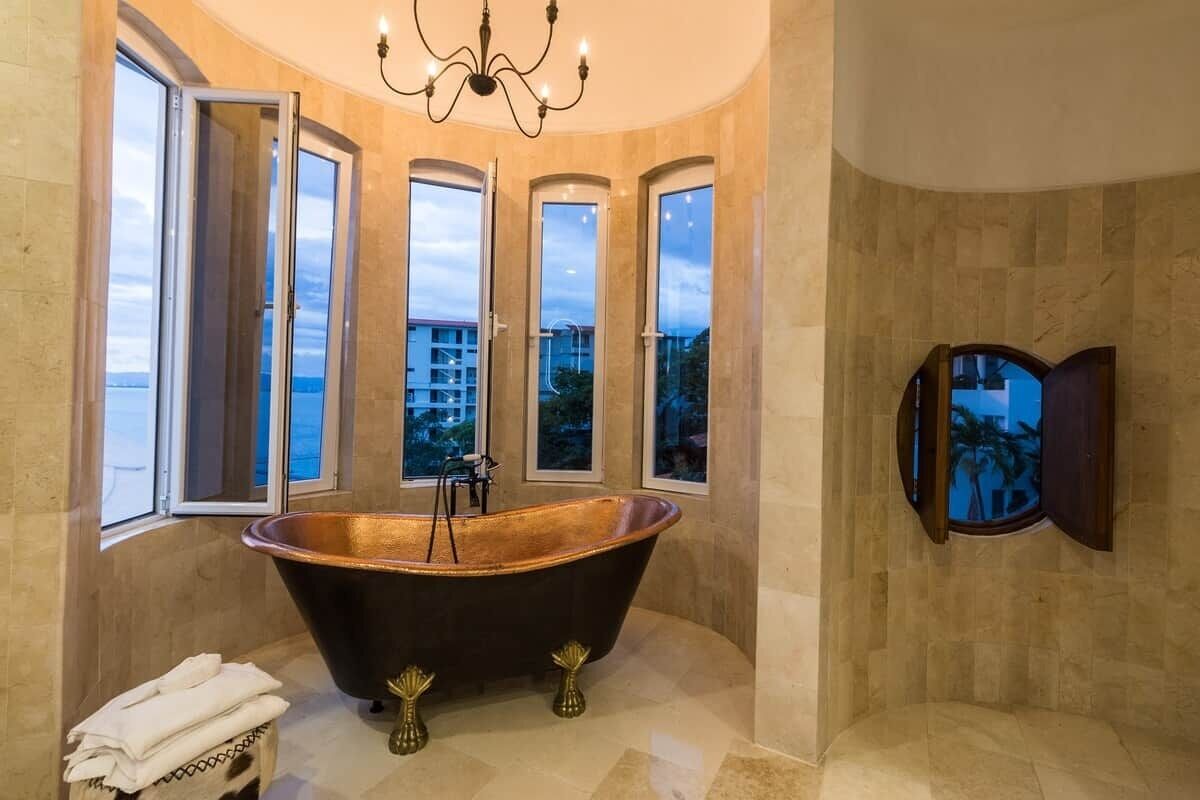 Ein Badezimmer mit freistehender Badewanne, großen Fenstern und einer Chandelier.