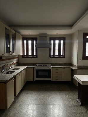 A kitchen with a stove, oven, two sinks, and a window with a decorative grille.