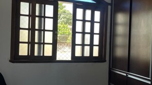 Un dormitorio con cama, ventana con contraventanas abiertas y armario.