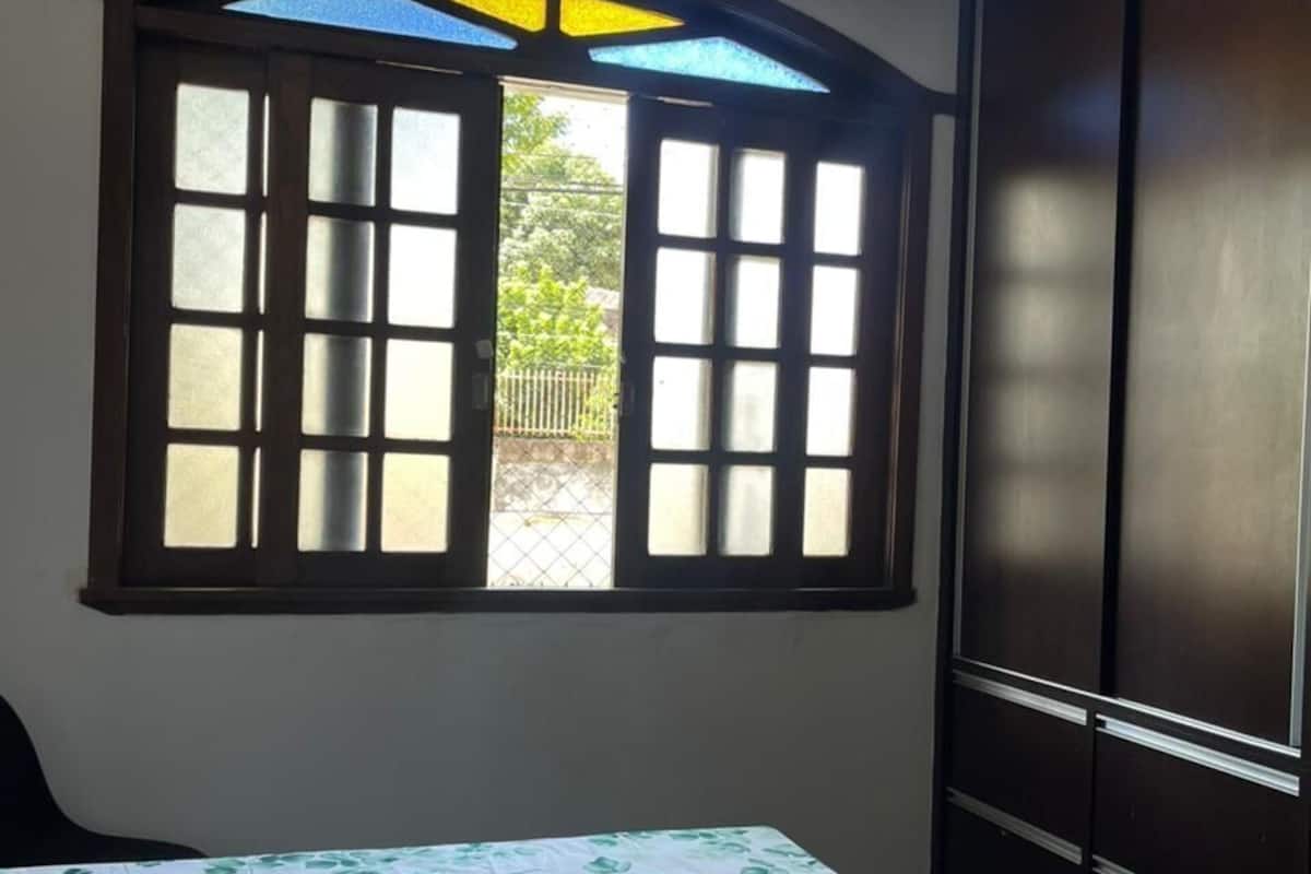 Ein Schlafzimmer mit Bett, Fenster mit geöffneten Klappen und einem Kleiderschrank.
