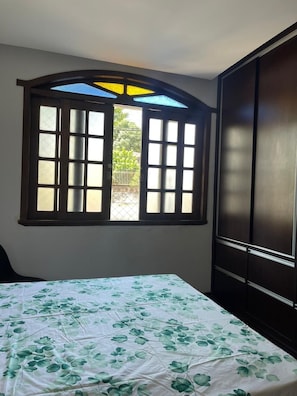 Une chambre à coucher avec un lit, une fenêtre dont les volets sont ouverts et une armoire.
