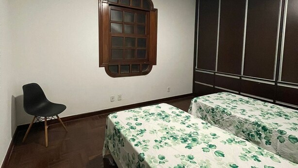 Un dormitorio con dos camas, una ventana, una silla y un equipo de aire acondicionado.