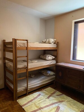 Una cama litera con escalera de madera, un aparador con cajones y una ventana con persianas.