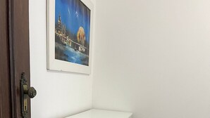 Un módulo de almacenamiento blanco con cajones, un pared blanca, una puerta de madera y un cuadro enmarcado encima.