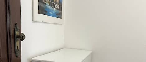 Un moble blanc amb calaixos adossat a una paret blanca, una porta de fusta i un quadre encastrat a la part superior.
