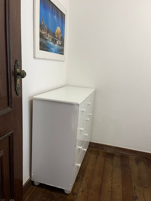 Un módulo de almacenamiento blanco con cajones, un pared blanca, una puerta de madera y un cuadro enmarcado encima.