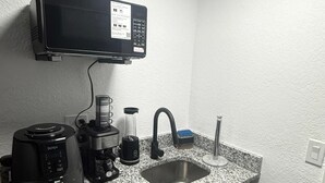 Keittiössä on mikroaaltouuni, kahvinkeitin ja leivänpaahdin työtasolla, pesuallas ja seinällä kyltti, jossa lukee ”Keittiö”.