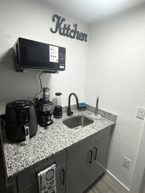 Eine Küche mit Mikrowelle, Kaffeemaschine und Toaster auf der Arbeitsfläche, einem Spülbecken und einem Schild mit der Aufschrift 'Küche'.