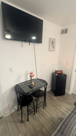 Ein Zimmer mit einem an der Wand befestigten Flachbildfernseher, einem kleinen runden Tisch mit Stühlen, einer Dekorationsvase und einem Heizgerät.