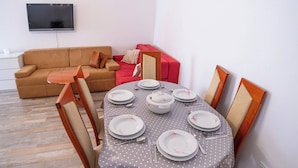 A dining area with a table set for four, a sofa, and a TV mounted on the wall. - Villa Hana in Historic Stolac (Stolac)