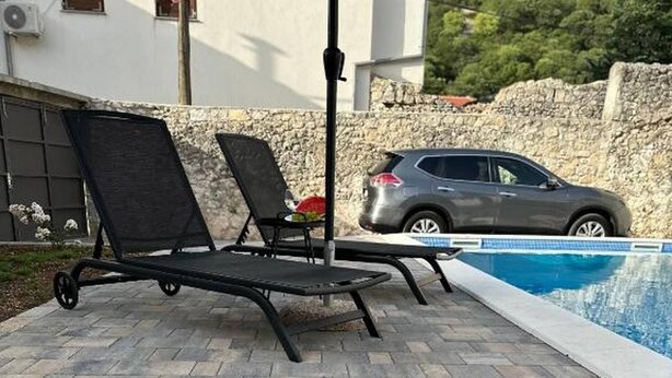 A poolside area with a tiled patio, two lounge chairs, a table, and a car parked nearby. - Villa Hana in Historic Stolac (Stolac)