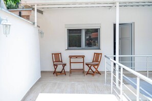 Un balcon avec une table et deux chaises, une fenêtre et une porte.