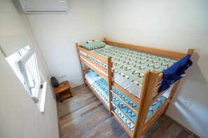 Un lit superposé avec une literie à motifs, une petite table avec une télécommande et une fenêtre avec des stores.