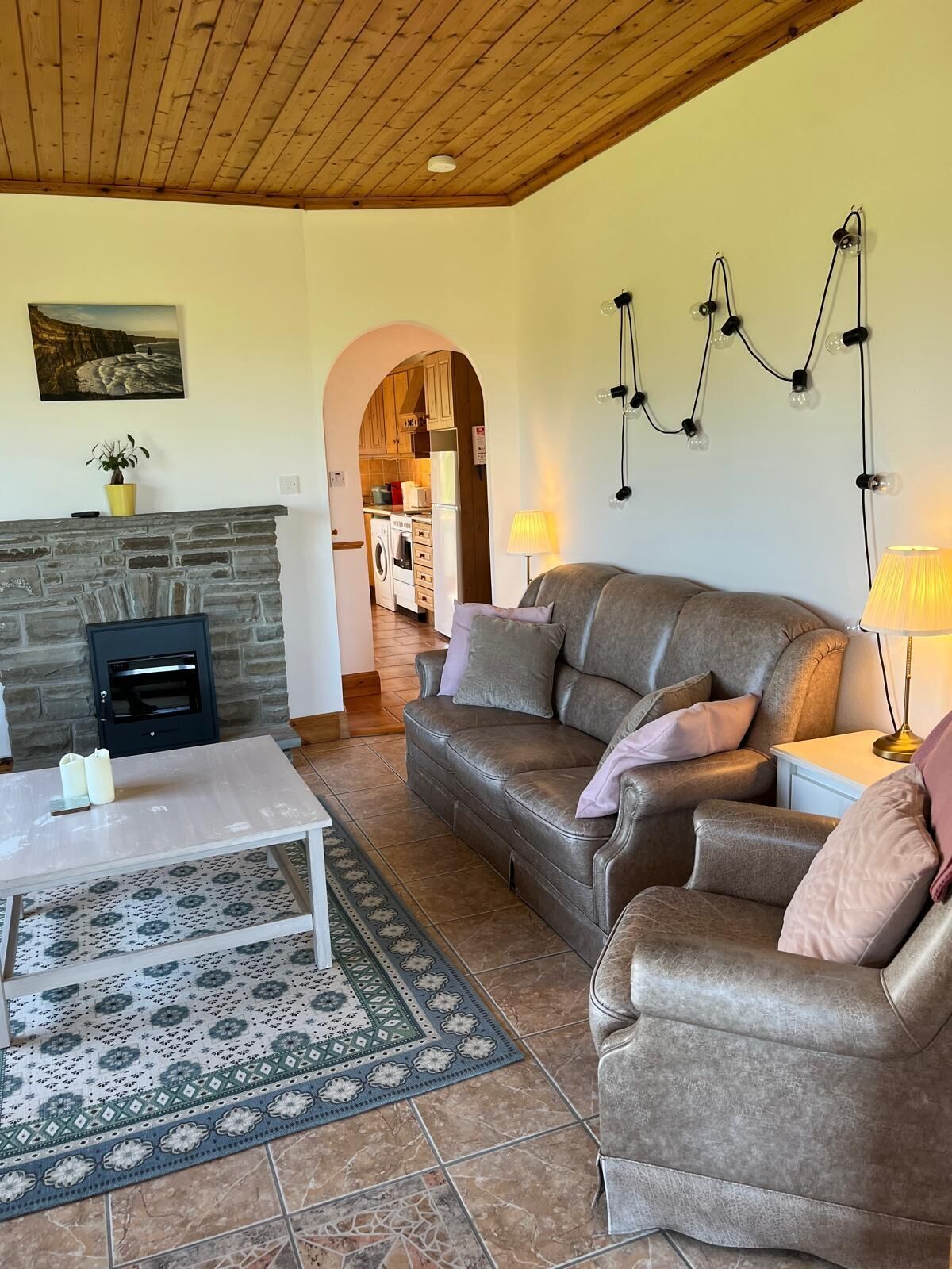 Ein gemütliches Wohnzimmer mit Kamin, Ledersofas, einem Couchtisch und einer durch einen Bogen sichtbaren Küche.