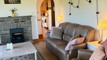 Ein gemütliches Wohnzimmer mit Kamin, Ledersofas, einem Couchtisch und einer durch einen Bogen sichtbaren Küche.