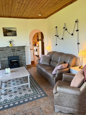 A cozy living room with a fireplace, leather sofas, a coffee table, and a kitchen visible through an archway.