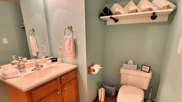 A bathroom with a wooden vanity, a toilet, a shelf with towels, and a striped rug.
