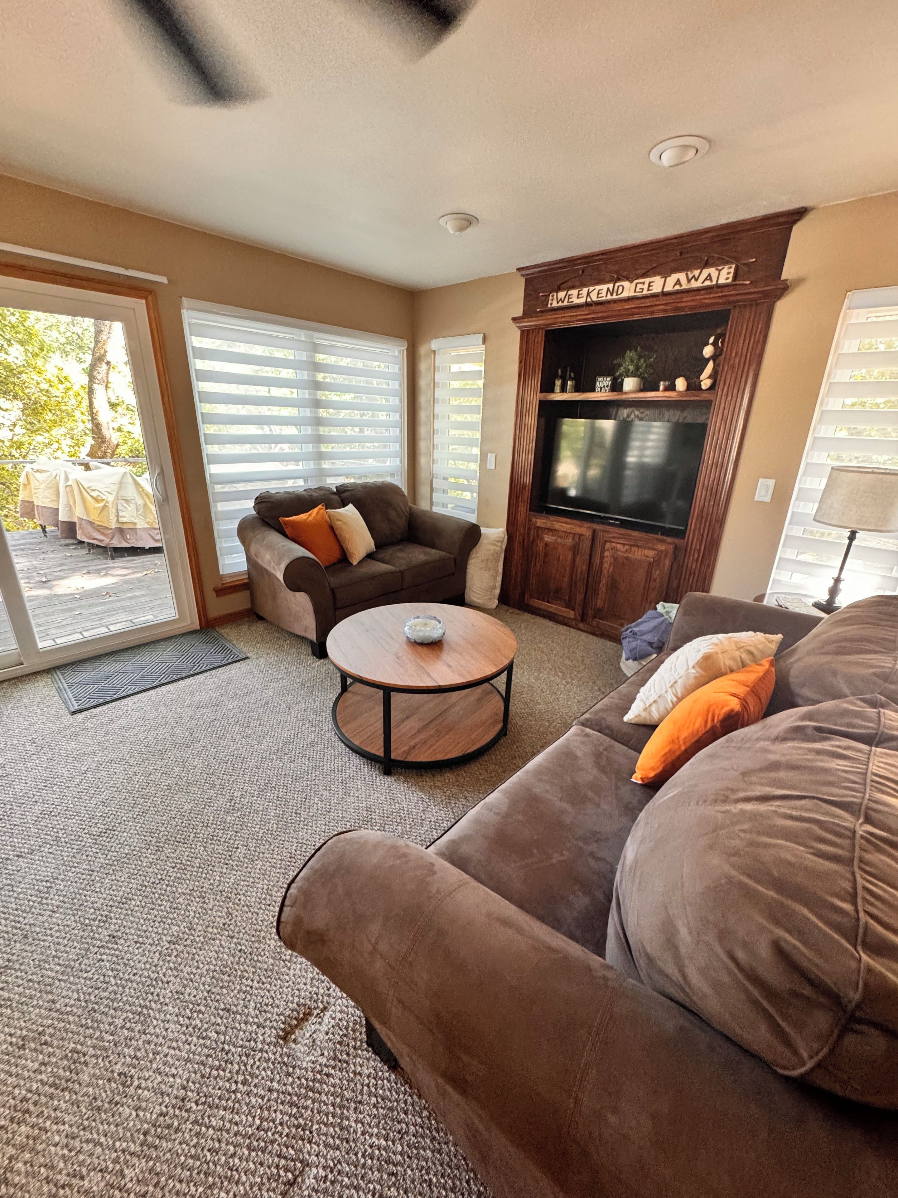 A living room with a brown sofa, a brown armchair, a round coffee table, and a flat-screen TV mounted on a wooden cabinet.