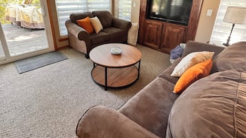 A living room with a brown sofa, a brown armchair, a round coffee table, and a flat-screen TV mounted on a wooden cabinet.