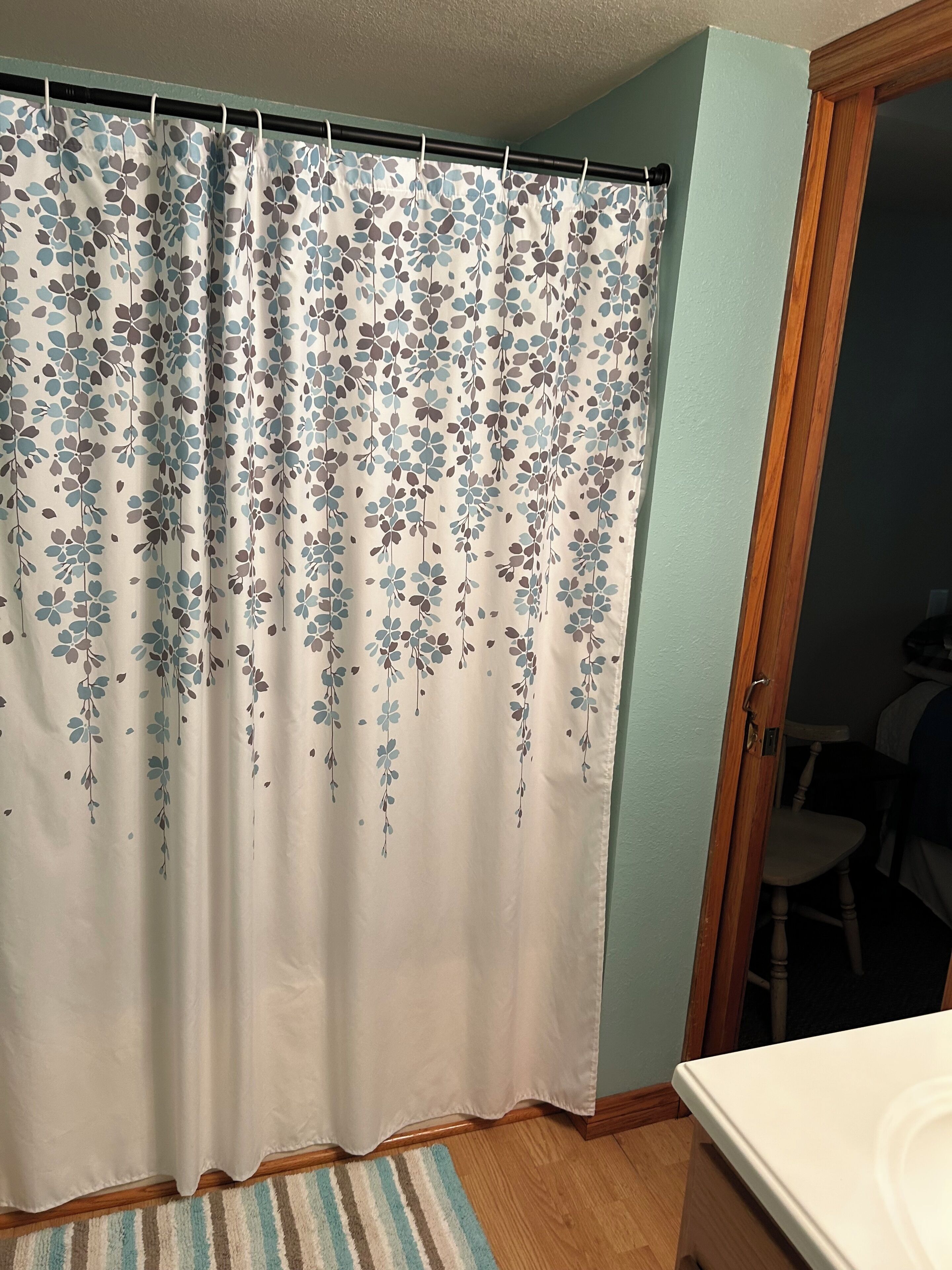 A bathroom with a shower curtain featuring a floral pattern, a wooden door, and a striped rug on the floor.
