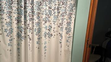 A bathroom with a shower curtain featuring a floral pattern, a wooden door, and a striped rug on the floor.