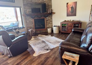 A living room with a stone fireplace, leather sofa, and a television mounted on the wall. - Rally Rider's Retreat! Paved Roads, large driveway & Centrally located (Spearfish)
