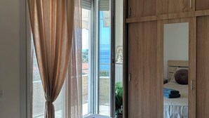 A bedroom with a bed, a large window with curtains, a wooden wardrobe, and a hanging light fixture. - Θάλασσα Thea (Kavala Paleo tsifliki)