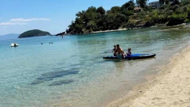 A beach with clear water, a small boat with people, and a distant island. - Θάλασσα Thea (Kavala Paleo tsifliki)