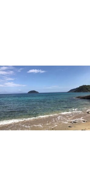 Une plage à l’eau claire, avec un rivage sablonneux et une île qui se profile à l’horizon.