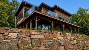 A modern wooden house with a stone retaining wall, large windows, and a balcony. - Chalet 2025 sur lac Barron navigable Spa, quai, 4 rooms -14 pers - Laurentians (Gore)