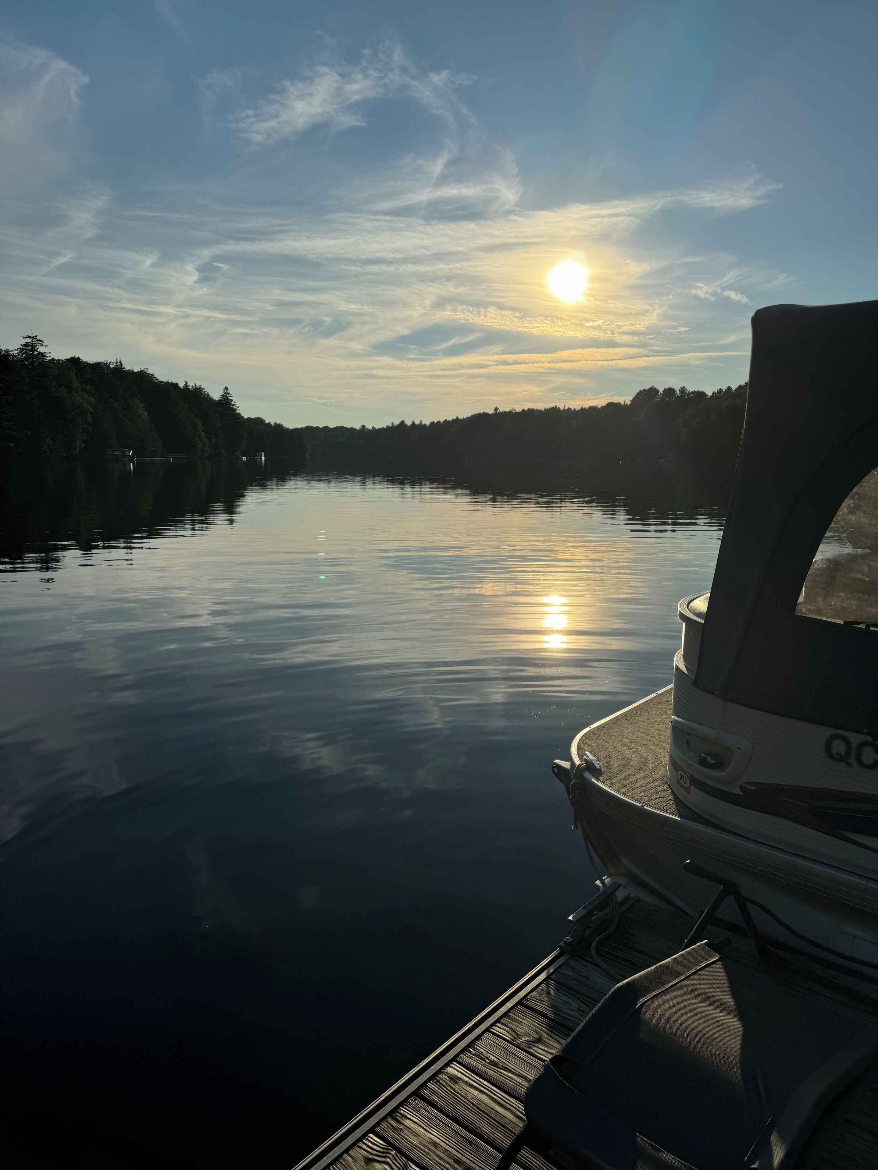 Un lac paisible, avec un bateau amarré sur la rive droite, entouré d’arbres et sous un ciel dégagé.