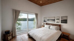 A bedroom with a large window, a bed, a bedside table, and a bench. - Chalet 2025 sur lac Barron navigable Spa, quai, 4 rooms -14 pers - Laurentians (Gore)