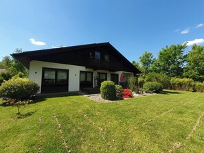 A modern two-story house with a sloped roof, a balcony, and a well-maintained lawn.