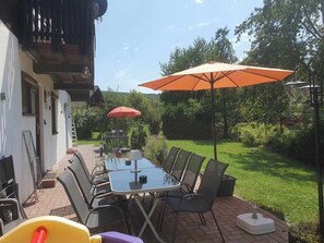 A patio with a table and chairs, an umbrella, and a view of a garden. - Vacation home Bussard am Silbersee (Frielendorf)