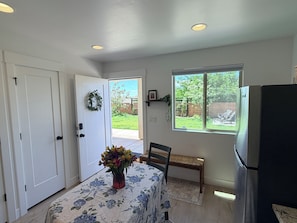 A kitchen with a refrigerator, a dining table with a floral tablecloth, a bench, and a window with a view of the backyard.