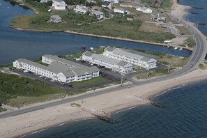 Eine Luftaufnahme eines Küstenhotels mit mehreren Gebäuden, einem Strand und einer Straße.