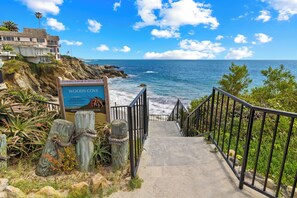 A coastal pathway leading to a beach with a sign indicating Woods Cove and a view of the ocean.