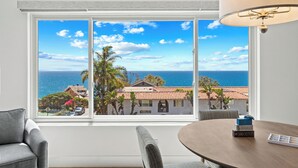 A room with a large window offering a view of the sea and buildings, a round table, and a chair. - Ocean View 2BR Condo in Laguna Beach, 1-Min Walk to Beach (Laguna Beach)