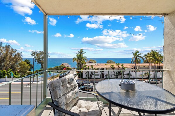 A balcony with a view of the ocean, a table with a bowl, and a chair.