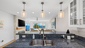 A kitchen with a double sink, granite countertop, pendant lights, and a view of the ocean. - Ocean View 2BR Condo in Laguna Beach, 1-Min Walk to Beach (Laguna Beach)