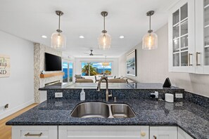 A kitchen with a double sink, granite countertop, pendant lights, and a view of the ocean.