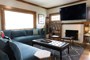 Ein Wohnzimmer mit Ecksofa, Couchtisch, Kamin, Fernseher und Bücherregal.