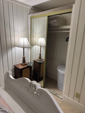 A bedroom with a bed, two bedside lamps, a dresser, a mirror, and a closet with a radiator.